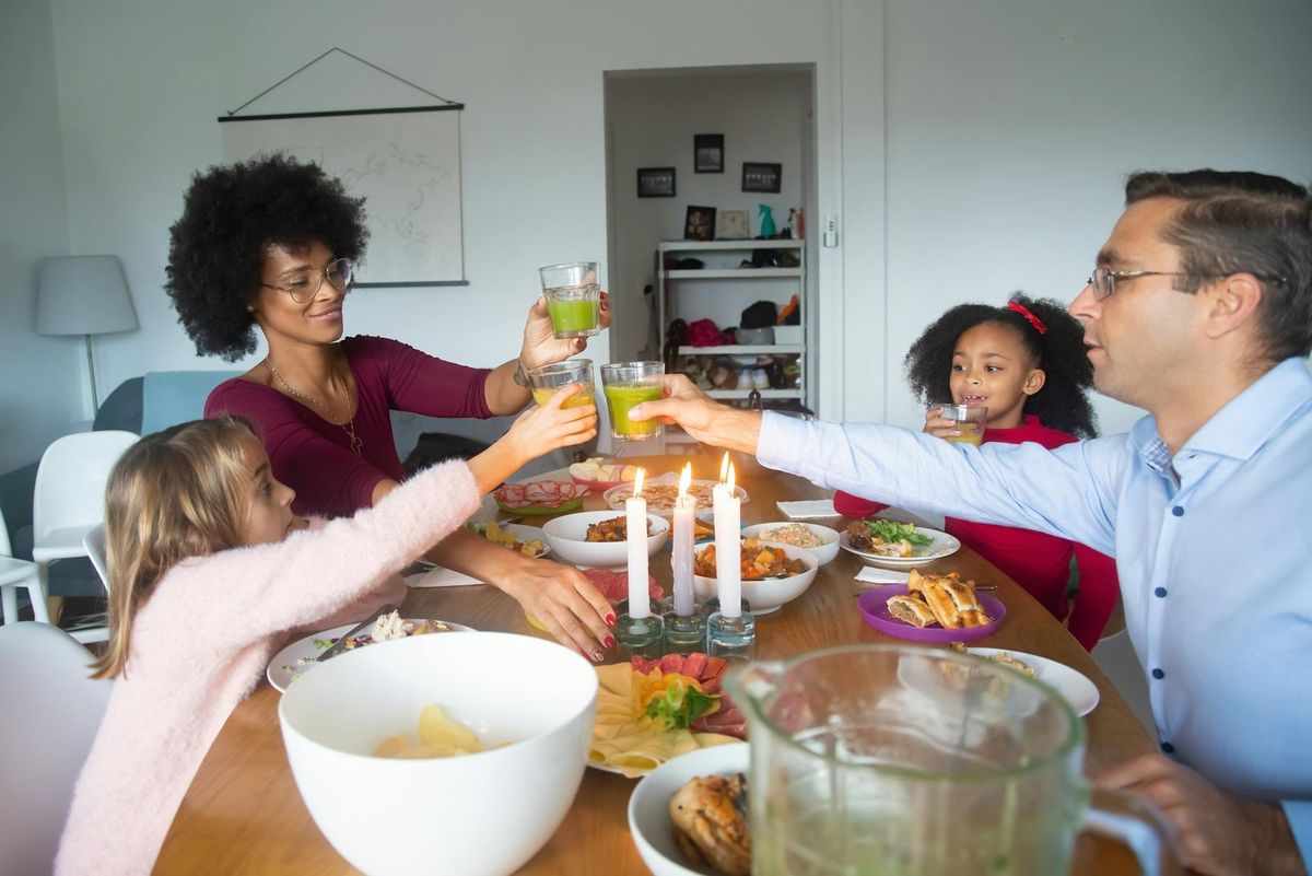 A diverse family celebrates with food and drinks around a candle-lit dining table at home.