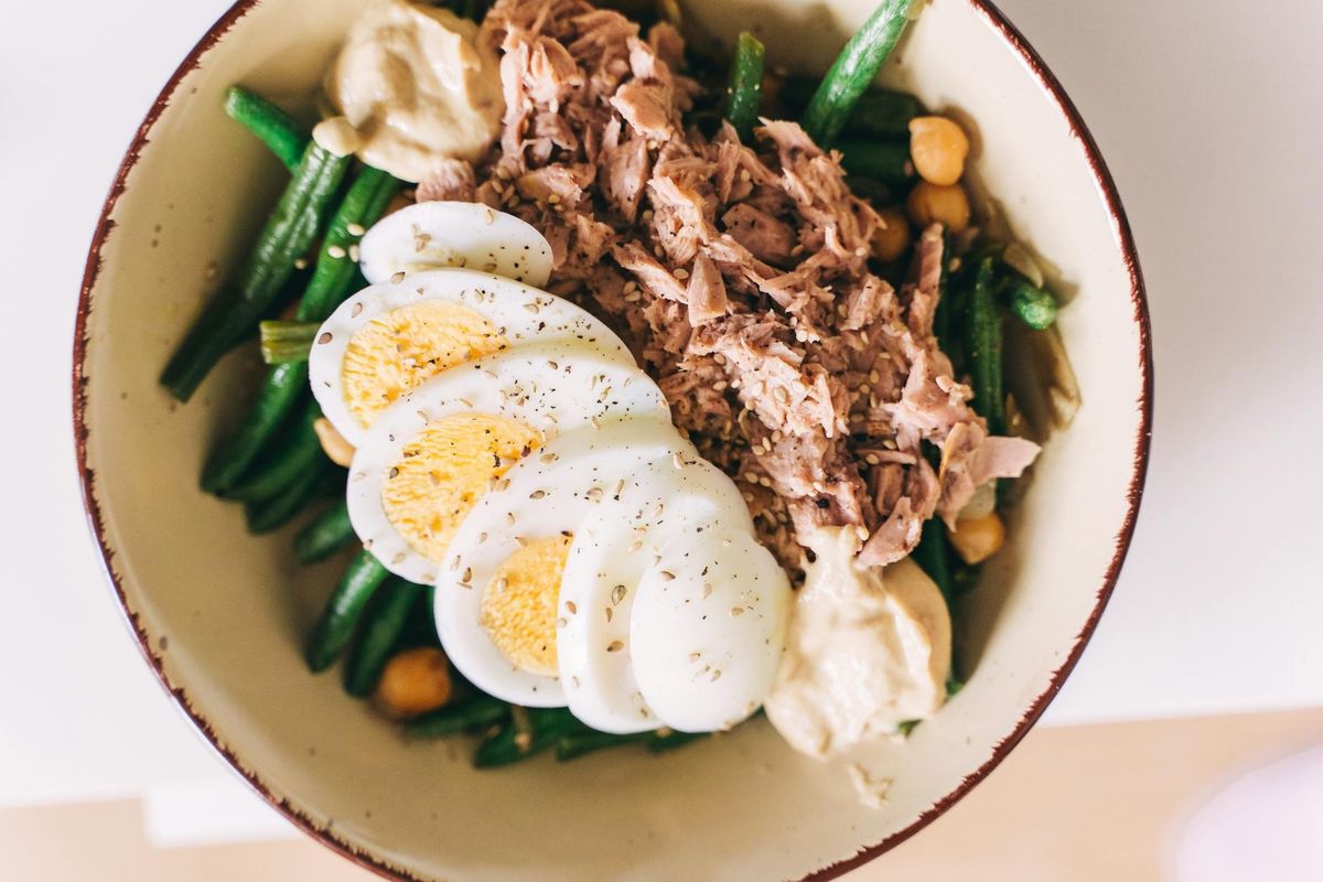 A protein-packed bowl featuring tuna, boiled eggs, green beans, and hummus — recovery fuel for active training.