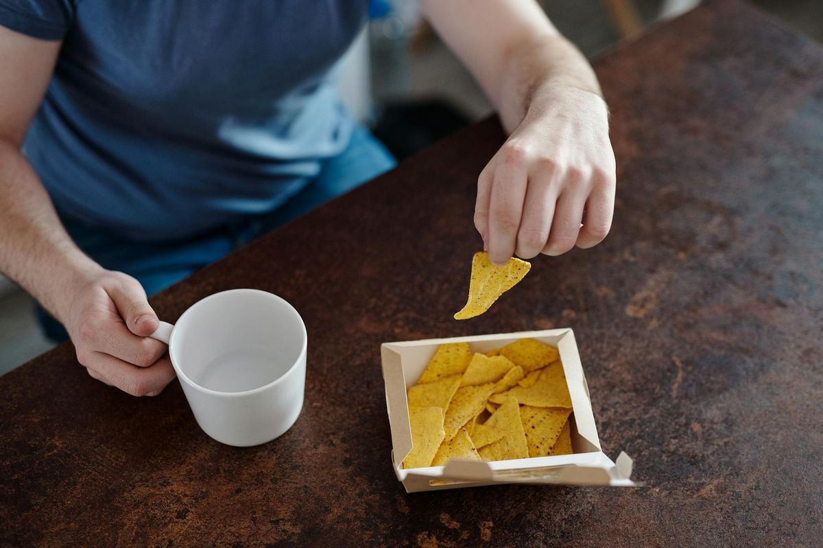 A man holding nachos and a ceramic cup.