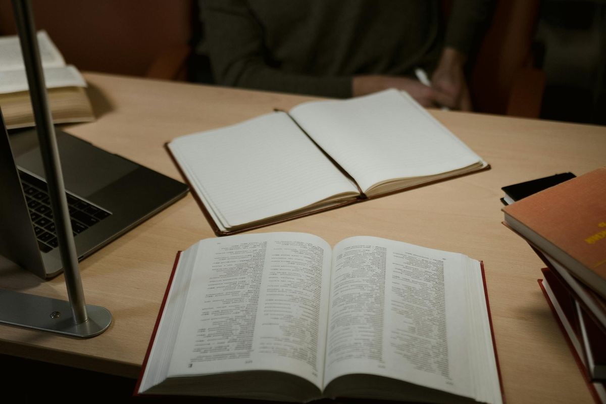 A warm indoor study setup featuring open books and a laptop on a wooden desk.
