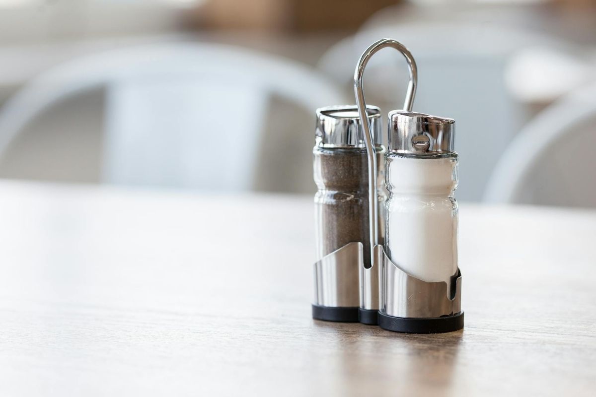Salt and ground black pepper shakers in stainless steel holder on table in restaurant on blurred background.