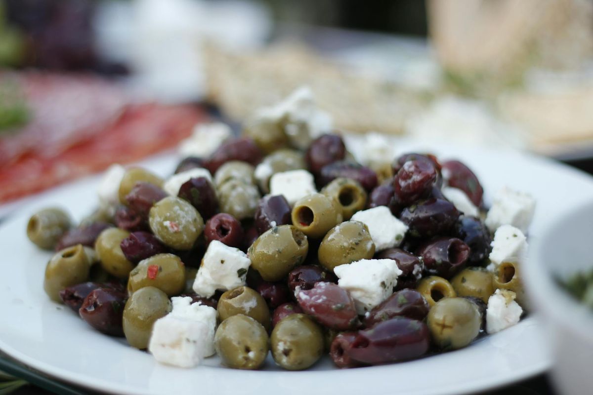 A close-up of a delicious olive and feta salad on a white plate.