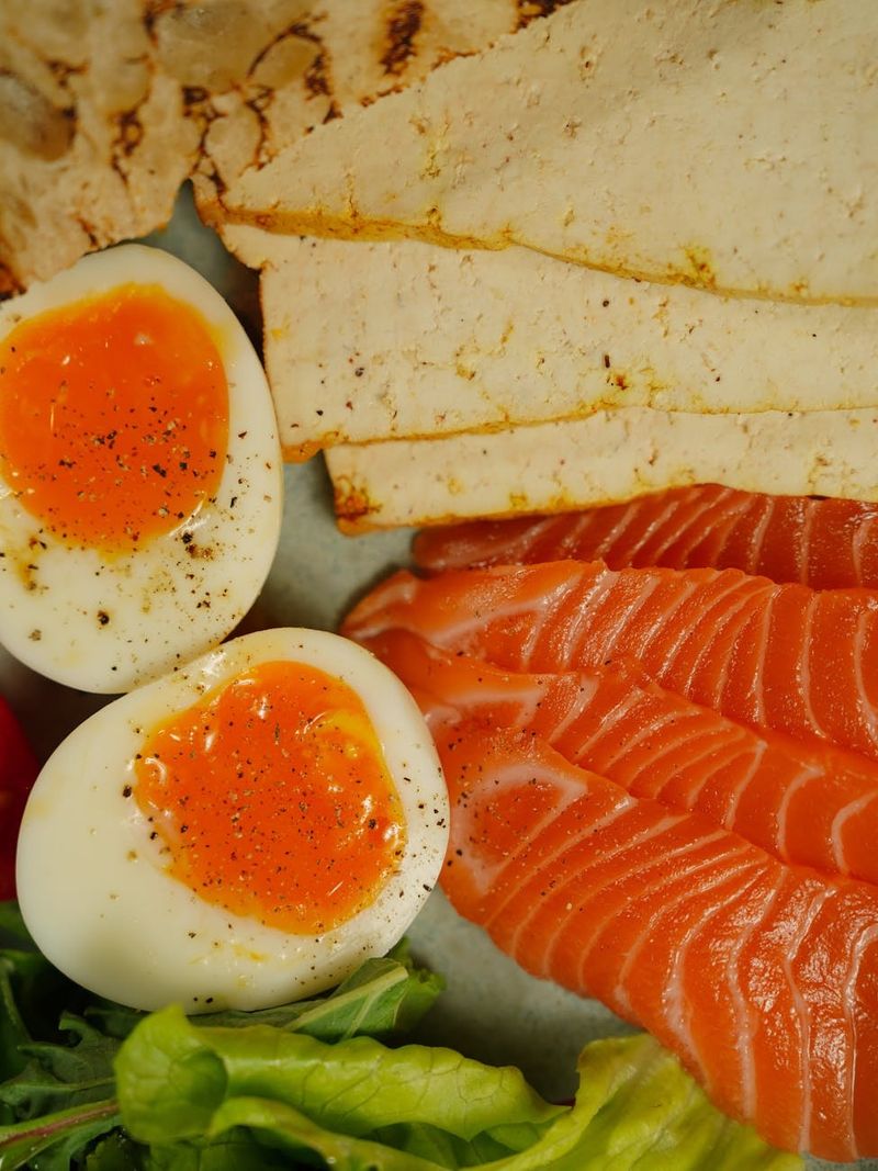 A delicious vertical shot of sliced salmon, boiled eggs, tofu, and greens.