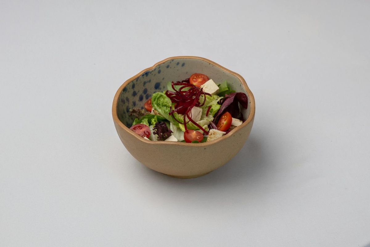 A vibrant mixed salad featuring tofu, cherry tomatoes, and greens in a ceramic bowl.
