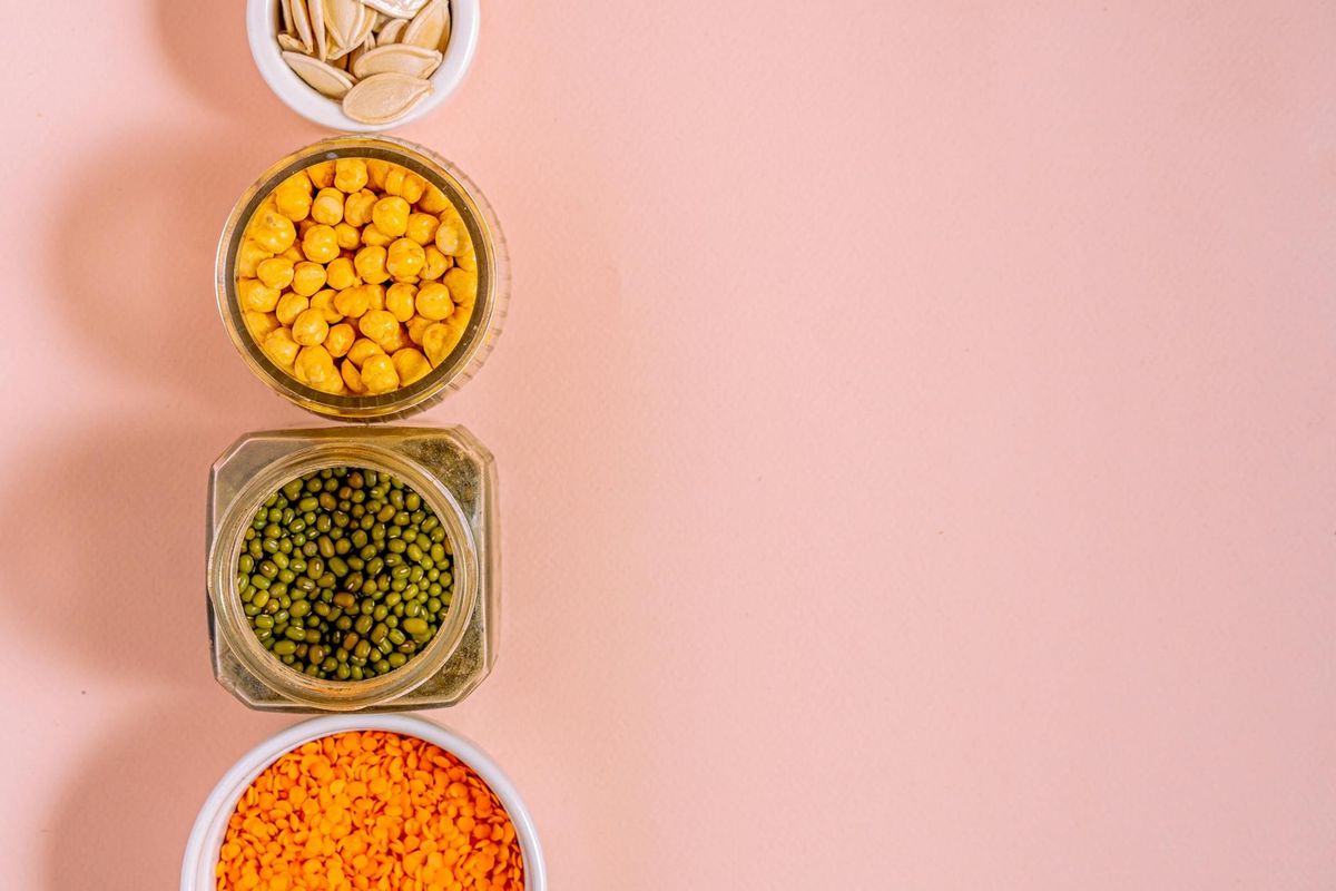 Chickpeas, lentils, mung beans, and pumpkin seeds with pink backdrop.