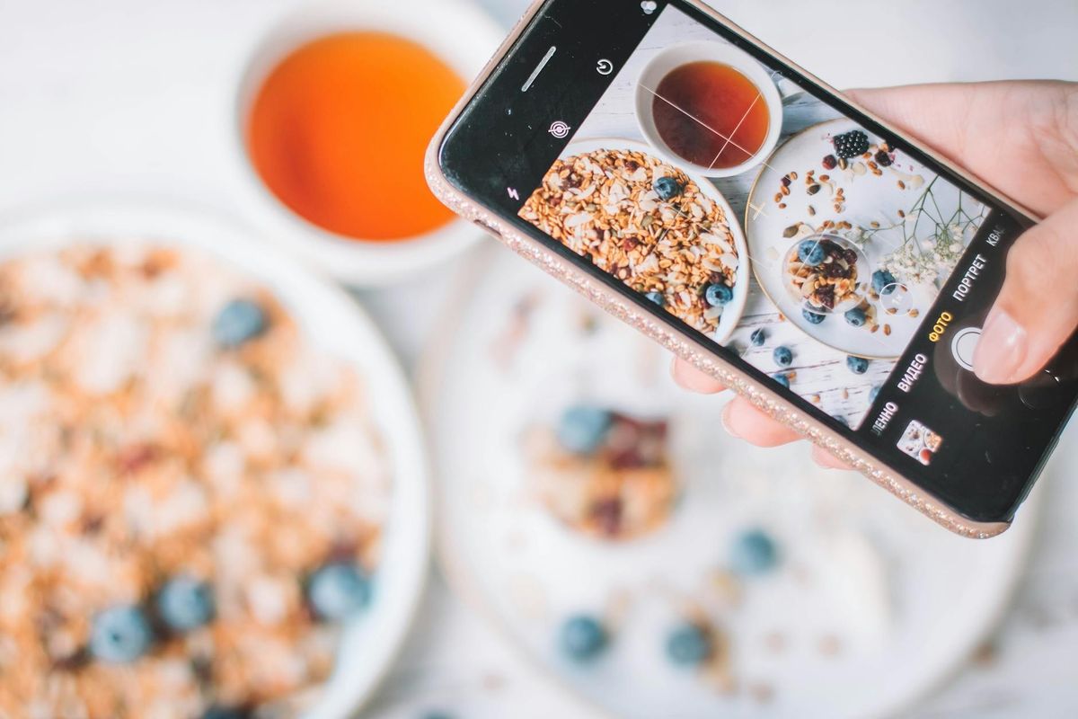 A smartphone capturing a healthy breakfast bowl with blueberries and tea — quick photo logging in action.