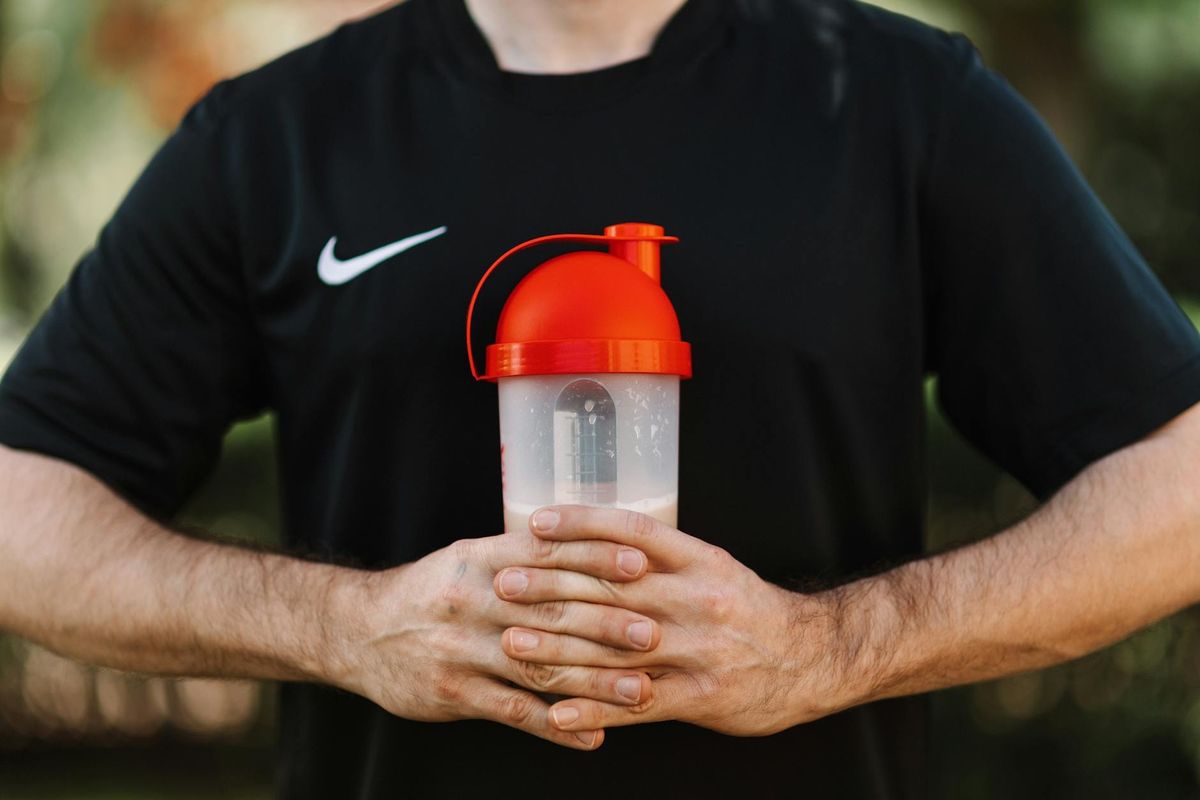 A man holding a protein shaker outdoors, wearing a black shirt.