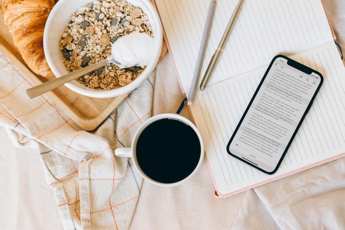 Breakfast with croissant, cereal, coffee, and phone resting on an open notebook.