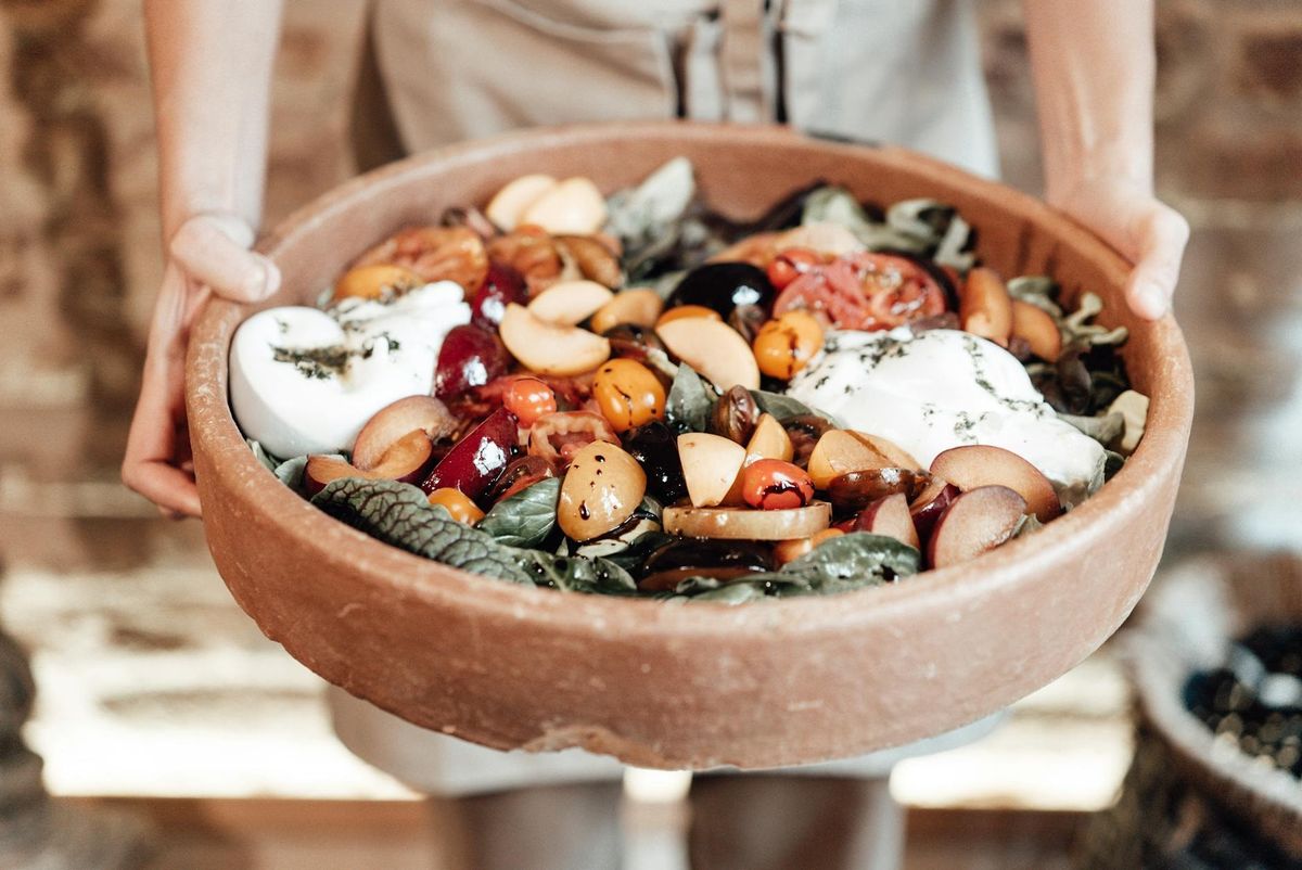 A vibrant rustic salad featuring fresh fruits, greens, and cheese in a wooden bowl.