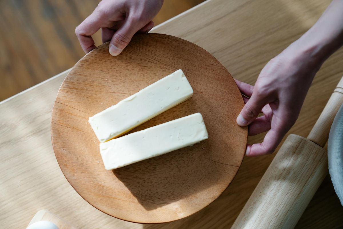 Hands holding a wooden plate with two butter sticks.