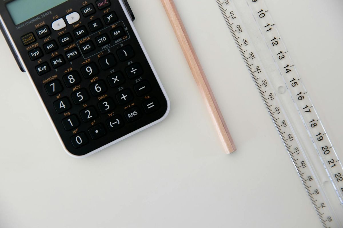 A calculator, ruler, and pencil arranged on a white surface.