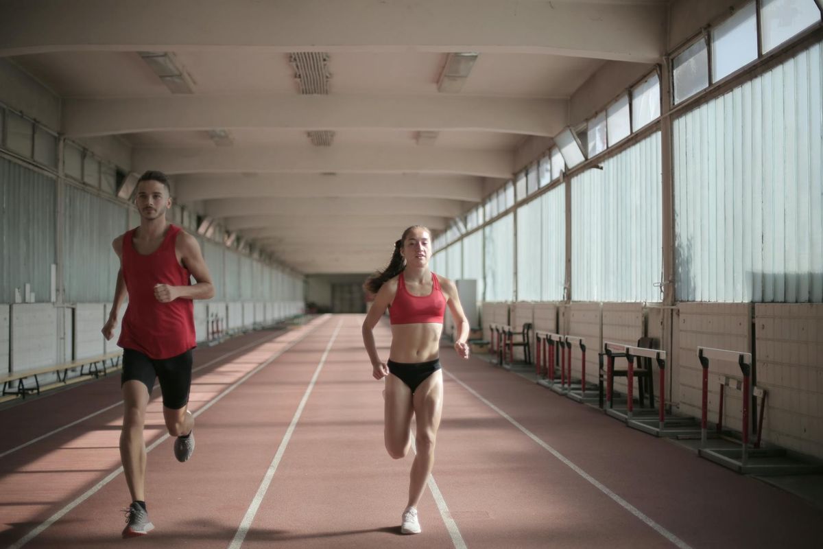 Male and female athletes running on an indoor track.