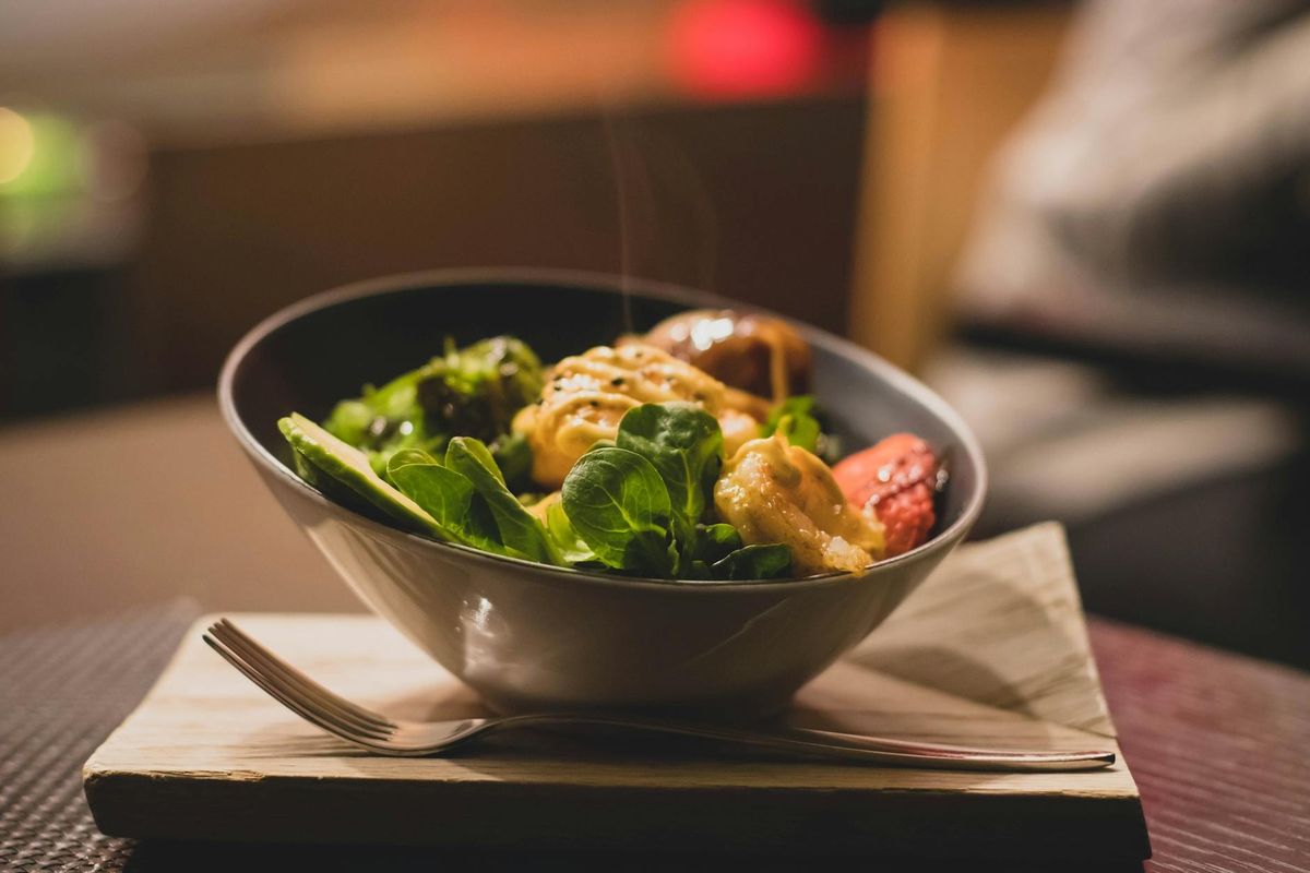Delicious bowl of salad with fresh greens and grilled chicken served on a wooden platter.