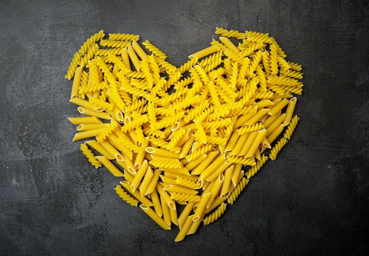 A creative heart shape made from fusilli and penne pasta on a black surface.