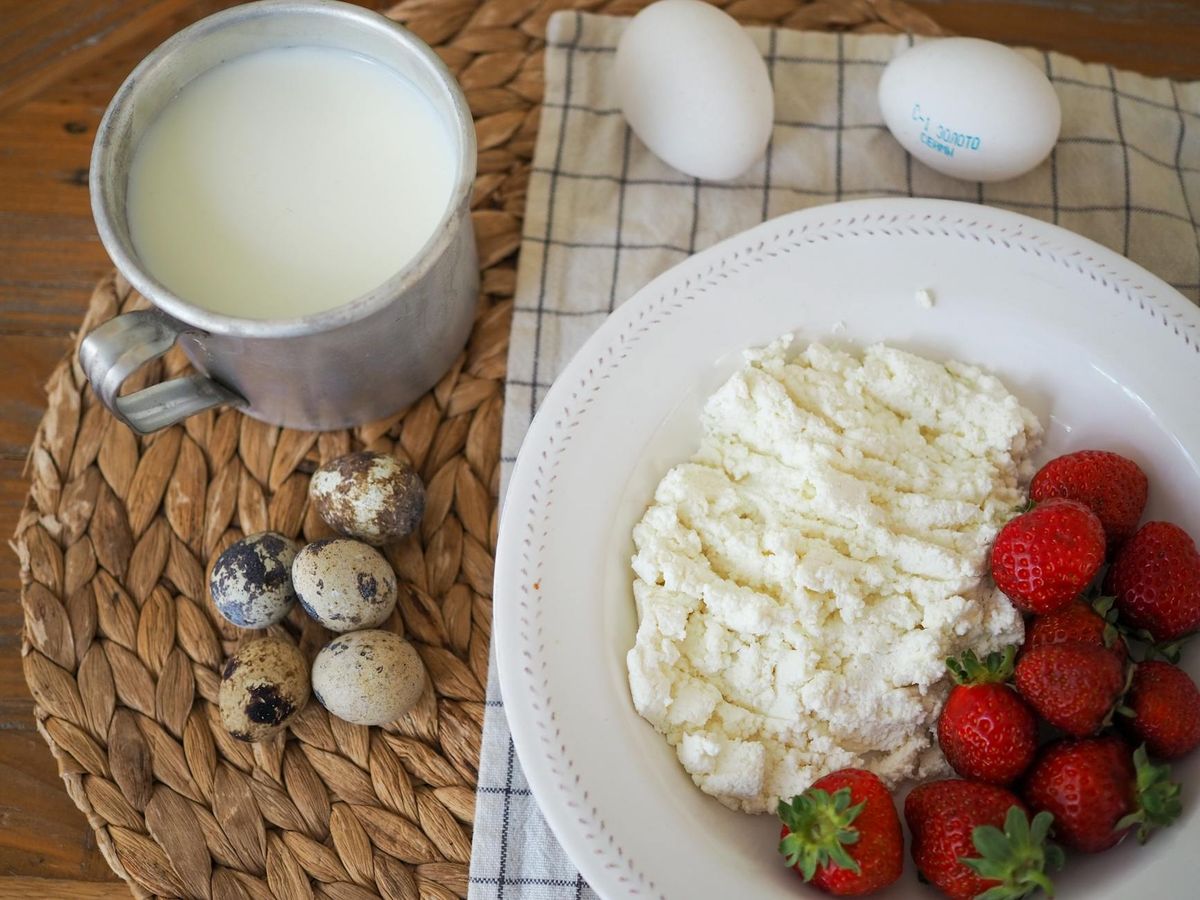 A rustic breakfast with milk, quail eggs, cottage cheese, and strawberries on a woven mat.