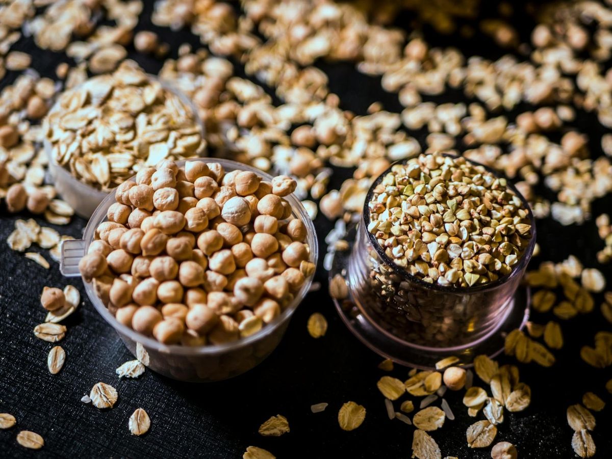 Assorted raw grains and seeds in cups on a dark background.