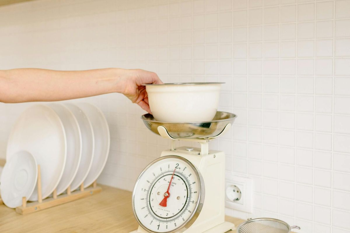 Hand placing a bowl on a kitchen weighing scale for food preparation.