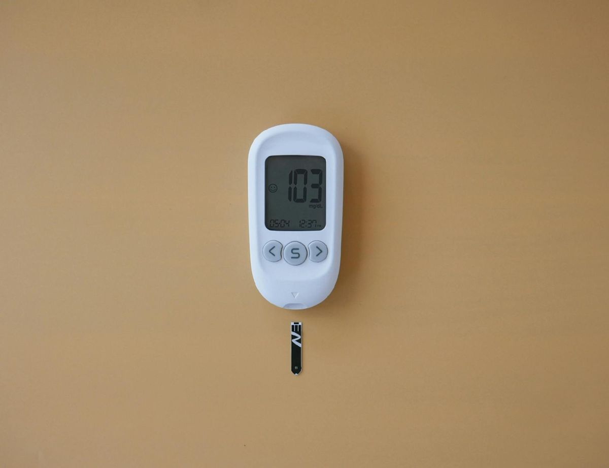 A digital glucose meter displaying blood sugar level on a brown surface.